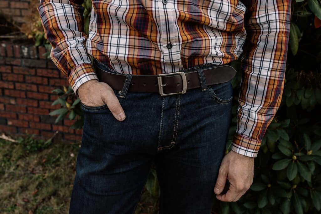 Man wearing a plaid button up shirt, dark blue jeans, and a dark brown full grain leather belt from Duvall Leather.
