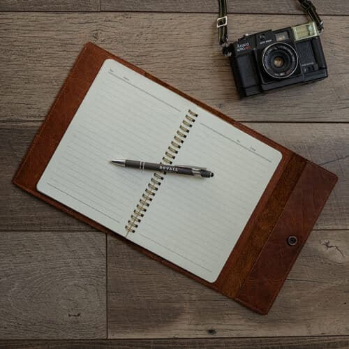 Brown Bison Leather Journal Cover with a notebook inside laid out on a wood surface with a gray Duvall Leather pen laying on top of the notebook.