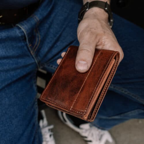 A man holding a closed brown bison bifold wallet with ID window in his hand.