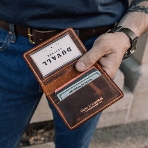 A man holding a brown bison leather minimalist wallet open to show the ID window and the card slots within.