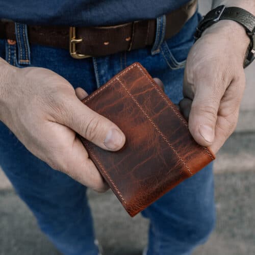 Man holding a brown bison leather bifold wallet in his hands.