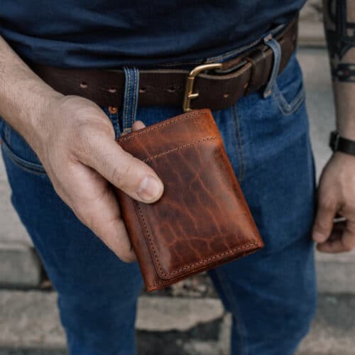 Man holding a folded brown bison leather trifold wallet from Duvall Leather.