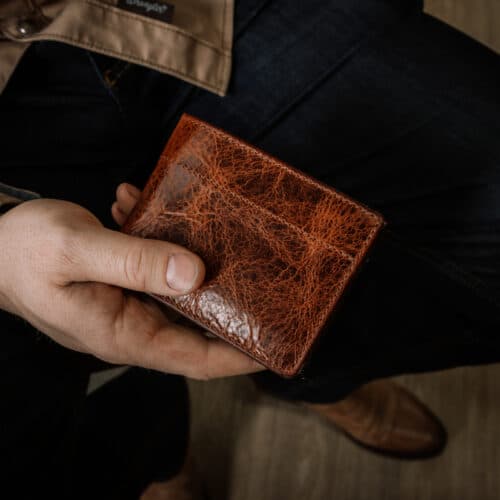 A man holding a closed Deluxe Bifold wallet with a brown bison leather cover to show the detail of the full grain leather and quality stitching.