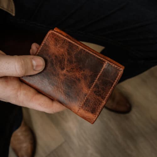 A closeup photo of a man holding a bison leather trifold wallet in his hand showing the detail of the full grain leather outside cover.