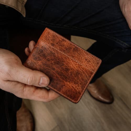 A closeup photo of a man holding a bison leather bifold wallet in his hand showing the detail of the full grain leather outside cover.