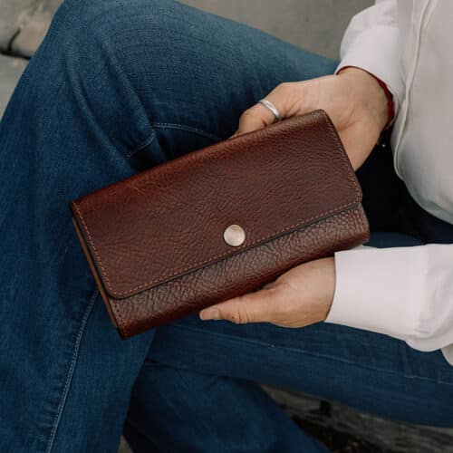 A close-up image of a woman's hands holding a closed red brown leather snap over wallet.