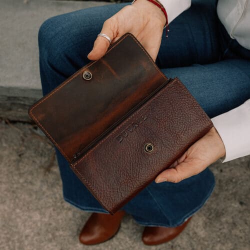 A close-up image of a woman's hands opening a red brown leather wallet, showcasing the snap closure of the wallet.